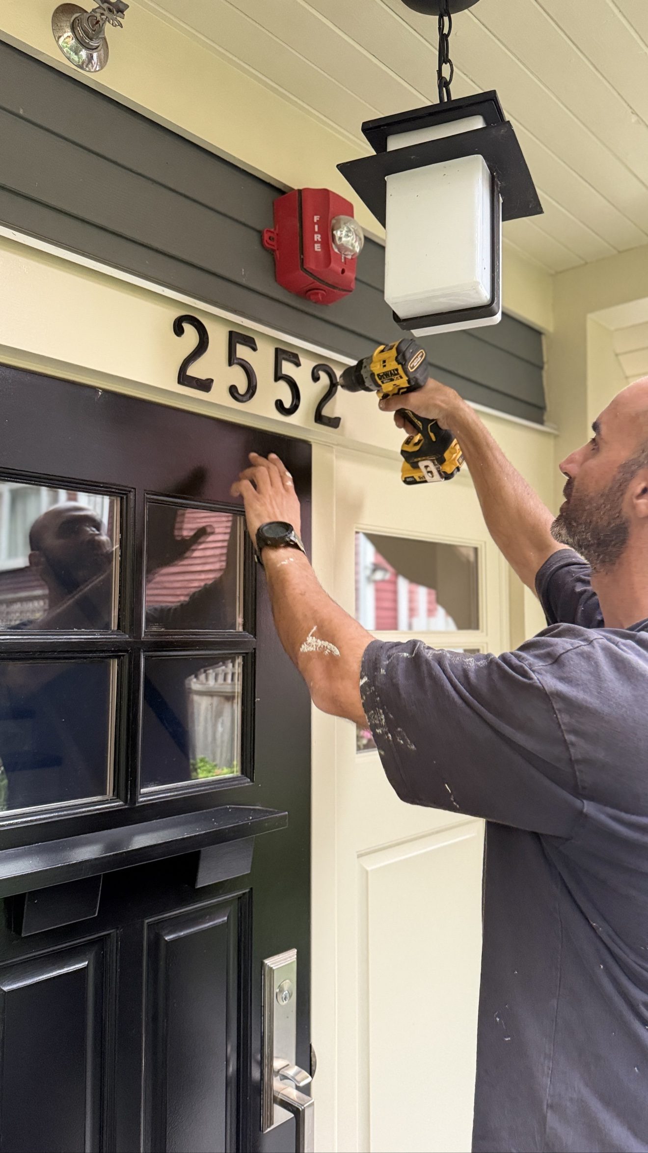 Farhad Niaghi installing house numbers with a drill on a residential entry